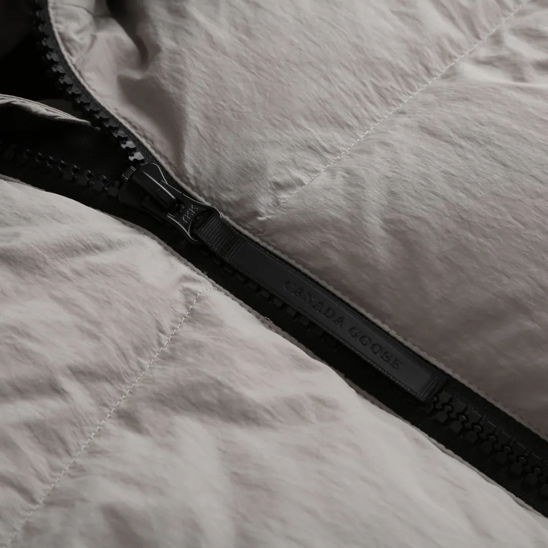 P980 Canada Goose hooded down jacket Fabric selection: Weaved with 400T high-count yarn. After special water-repellent treatment, the surface forms a lotus leaf effect - raindrops will slide down in beads, and snow particles will fall off when touched. The tear resistance reaches 200N (approximately 20kg load-bearing), the light gray matte texture breaks the stereotype of "outdoor clothing = hardcore", and the soft luster presents a high-end matte effect under urban neon lights, seamlessly switching scenes from ski resorts to CBD office buildings.  Process 1: Use polyester woven ribbons as the base, and use high-precision computer embroidery to decorate the brand letters on the ribbons. The edges of the pattern are clear, the stitches are fine and even, and multiple layers of embroidery threads are stacked to enhance the three-dimensional effect.  Process 2: Precision thread reinforcement to prevent velvet drilling and ensure that the fluffy and resilient elasticity lasts as new.  Details: The embedded cuffs are three-dimensionally woven to form a "wavy" elastic structure, forming natural folds when fitting the wrist, increasing the contact area with the skin, thus improving the windproof effect. At the same time, micro-velvet treatment is added to the inside of the cuffs, which feels like a second layer of skin and avoids friction on the skin from metal zippers or hard fabrics.  90 national standard high-quality white duck down: selected high-loft down, weighing 240g, light and warm, with excellent temperature locking performance and good resilience.  Accessories: 1:1 customized armband, 1:1 customized zipper pendant, 1:1 customized elastic buckle, etc. SIZE: S M L XL